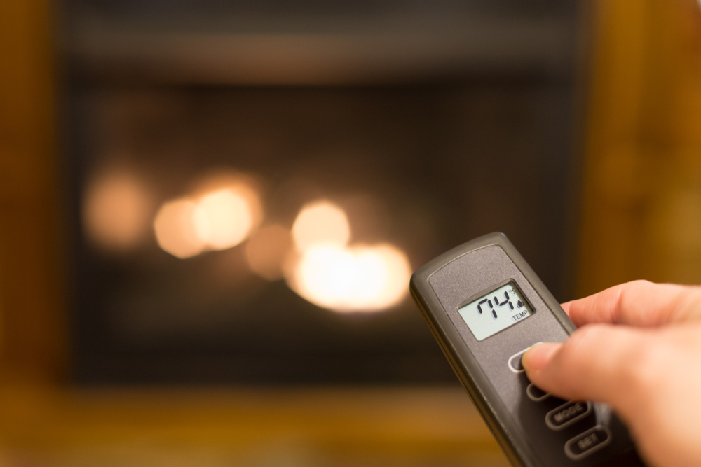 Hand changing temperature with remote in front of a fireplace