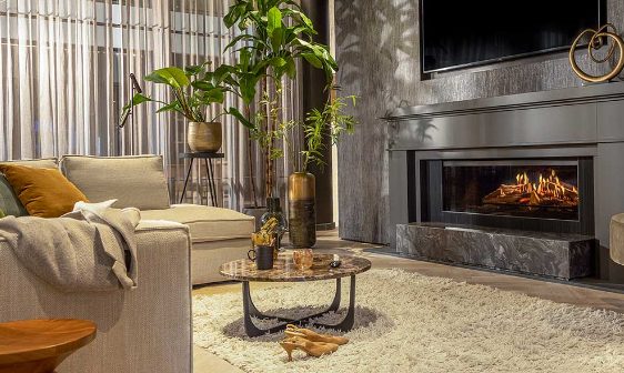 An electric fireplace in a living room with a tan couch and orange pillows on the couch.