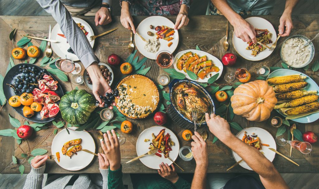 several hands reaching over a grilled food spread, taking food