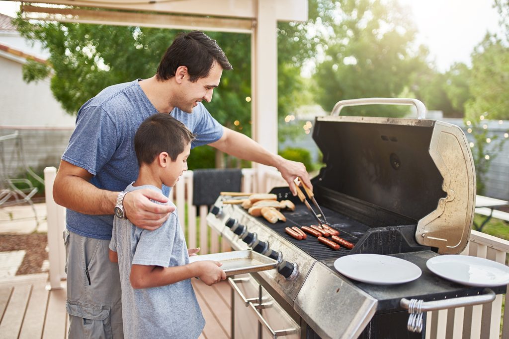 A father and son using a grill on their deck.