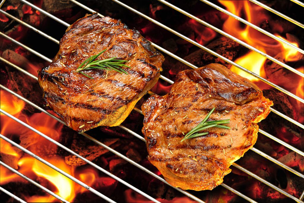 Grilled pork steaks on a flaming grill.